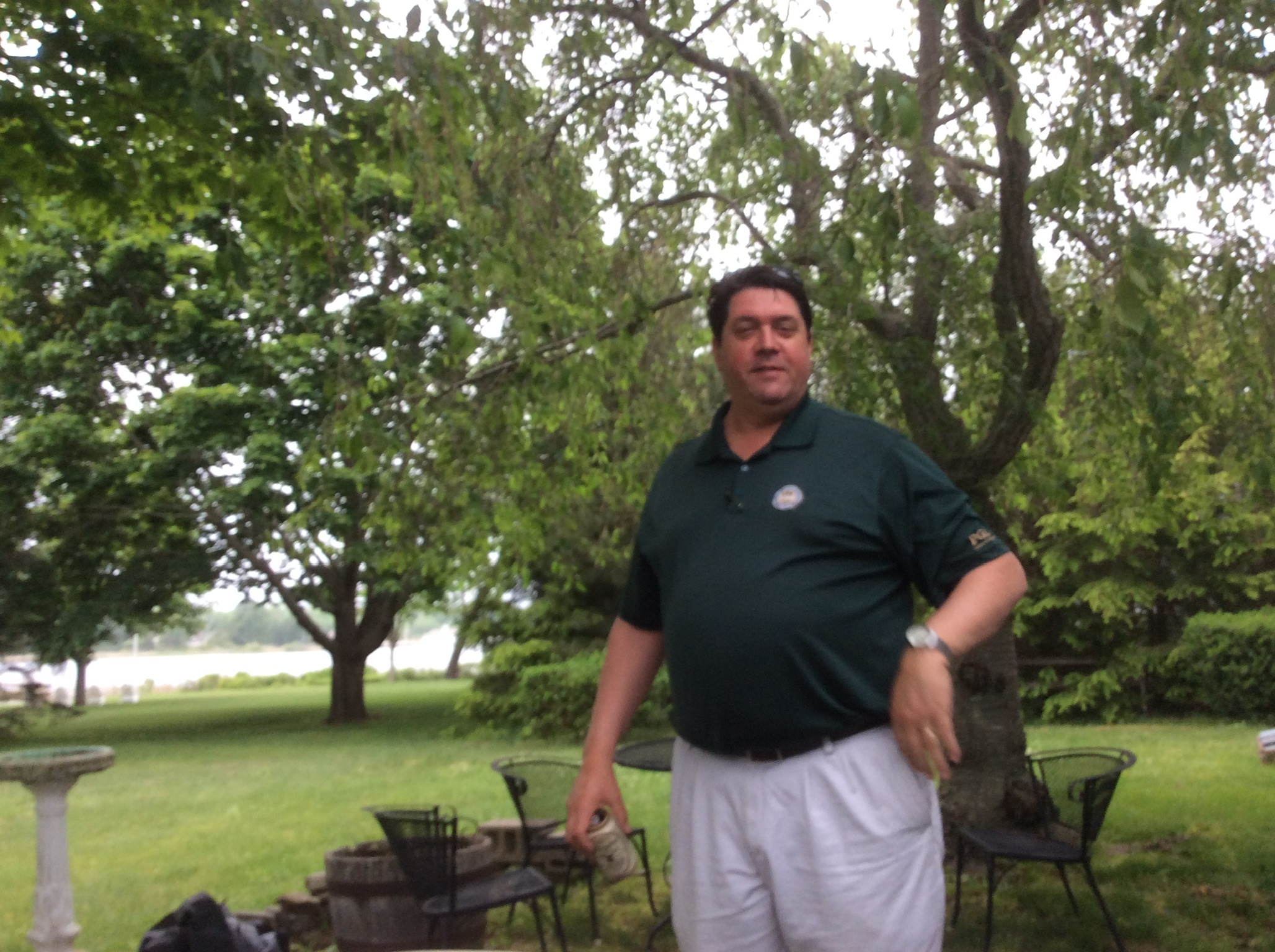 Todd standing outdoors beneath leafy trees in a dark green shirt.